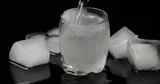 Pour vodka into icy glass with ice cubes placed on a black background