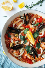 close-up of seafood paella and tomato sauce in a pan on a light background
