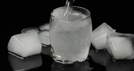 Pour vodka into icy glass with ice cubes placed on a black background