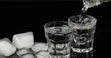 Pour vodka into shot glasses with ice cubes placed on a black background