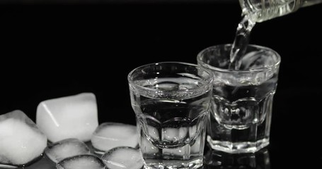 Pour vodka into shot glasses with ice cubes placed on a black background