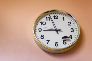 Round clock hanging on the pink wall. Time is now five minutes to nine