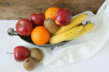 apples, oranges, kiwi, bananas in basket on wooden table