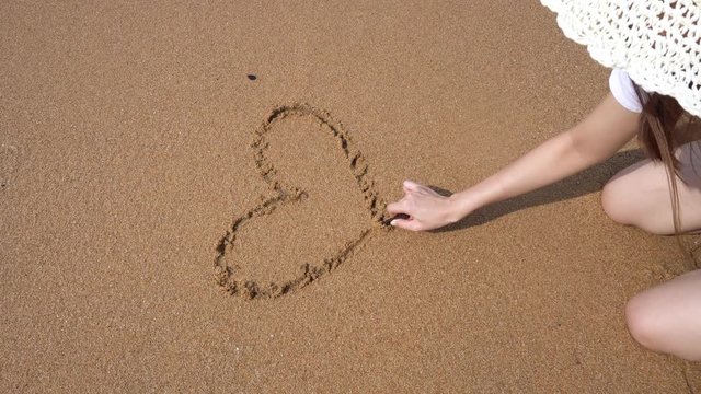 Happy girl draws a heart on a sandy beach