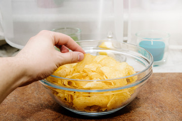 The hand pulls potato chips. Chips pulled from a salad bowl. Concept of eating delicacies, relaxation. Unhealthy food causing overweight and cholesterol problems.