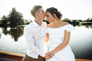 Happy stylish couple hugging and kissing near the lake during sunset