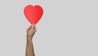 The hand lifts the heart up. The concept of showing love and expressing one's feelings. Red heart on a gray background. Positive emotions towards another human being.