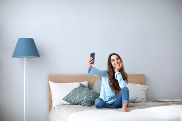 Beautiful happy woman at home on the couch do selfie on cell phone.