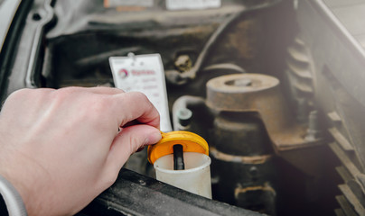 The man unscrews the washer fluid reservoir. The concept of car care for liquids, replenishing windscreen washer fluid. Taking care of travel comfort and safety while driving.