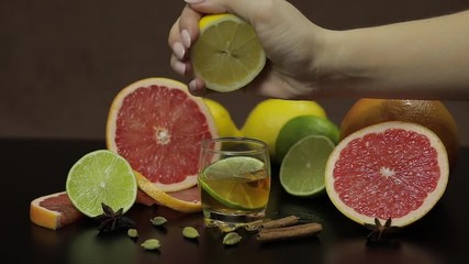 Woman squeezes juice from lemon into a glass cup with alcohol cocktail