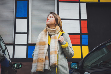 Style girl in scarf and coat stay between cars