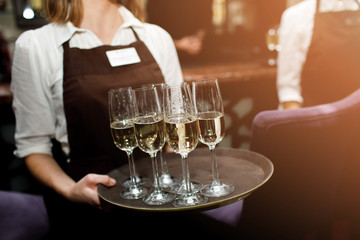 Full glasses of champagne on tray. Female waiter in uniform serving champagne.