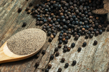 heap of black pepper and black pepper powder, milled peppercorns on wooden background, dried spice...