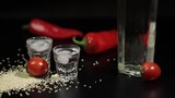 Sparse sesame seeds to two cups of vodka near bottel with vodka
