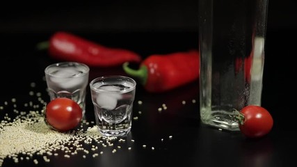 Sparse sesame seeds to two cups of vodka near bottel with vodka