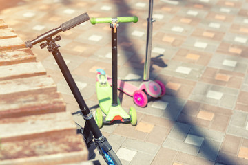 Three children scooter parked at park area on bright sunny day. Different types of scooter stand...