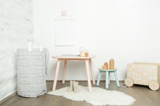 Nicely decorated kids room in pastel colors, wooden toys, furniture and blank white poster on the wall