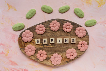 SPRING word and flower cookies on a wooden board on a pink background . Spring holidays cooking concept.