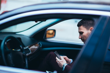 Young businessman looking at his cellphone while comfortably sitting at the front seat in his luxury limo.