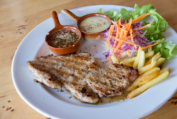 Grilled pork steak and vegetables . plate of grilled pork with french fries and salad on Table. juicy grilled pork chop (neck cut) with greens. meat steaks with vegetables and greenery on table .
