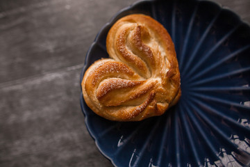 Heart-shaped bun with powdered sugar and cinnamon on a wooden background in a rustic style. Selective focus.