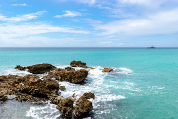 Sunny day on beautiful tropical blue ocean with waves crashing against sea rocks