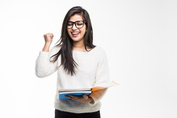 Portrait of attractive indian student woman standing holding reading a book with win gesture over white background. Education test exam thinking concept
