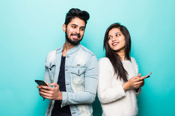 Indian couple standing back to back and holding mobile phone isolated on green background