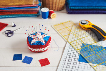 Pin cushion stylized elements of American flag, stacks of fabrics, quilting accessories