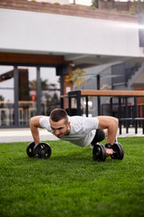 Fototapeta premium one young man,20-29 years old, doing push ups with weights in a beautiful backyard of a fancy house.