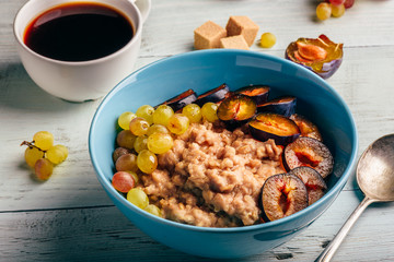 Porridge with fresh plum, green grapes and cup of coffee.