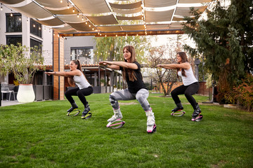 three young ladies,20-29 years old, doing squats in jump boots in a backyard of a a fancy house.