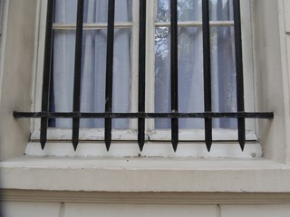 black forged security grille in front of a window, the wooden frame and the house wall painted...