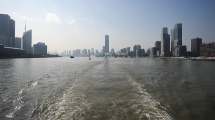 shanghai bund viewed from ferry ship, skyscrapers and landmarks with blue sky background, cargo ships sailing on Huangpu river, Ship wake on the river, Water foam trace behind ship goes, slow motion.