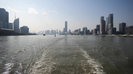 shanghai bund viewed from ferry ship, skyscrapers and landmarks with blue sky background, cargo ships sailing on Huangpu river, Ship wake on the river, Water foam trace behind ship goes, slow motion.