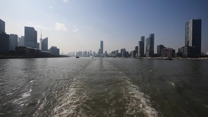 shanghai bund viewed from ferry ship, skyscrapers and landmarks with blue sky background, cargo ships sailing on Huangpu river, Ship wake on the river, Water foam trace behind ship goes, slow motion.