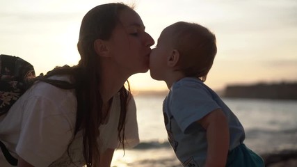 Mom kisses a little baby and he reaches out for her at sunset in slow motion