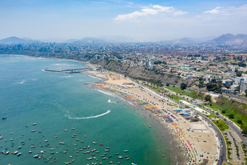 Lima, Peru - March 17 2019: Aerial view of Agua Dulce beach in the district of Chorrillos. Lima's coastal shoreline with blue ocean. Summer day, people relaxing having fun.