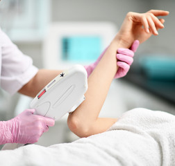 Closeup. Doctor-cosmetician in gloves performes a procedure on patient's hand with medical equipment laser in equiped beauty shop