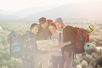 Group of people hiking and looking at map during their adventure. Two men and two women, hikers exploring mountains. Happy friends with backpacks using map to choose right direction.