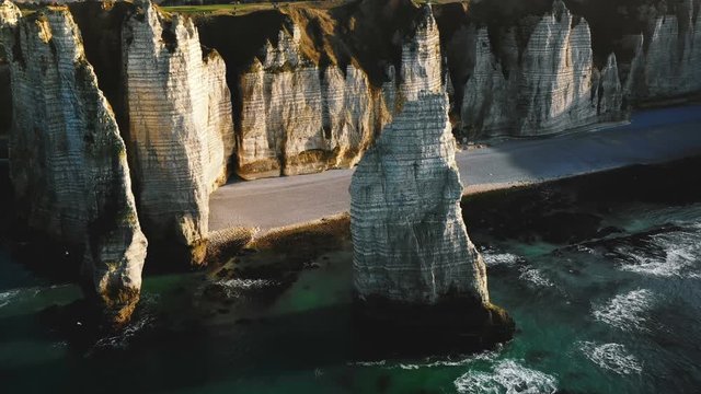 Drone flying above epic natural alabaster rock arch and pillar at famous white seaside cliffs of sunny Etretat Normandy.