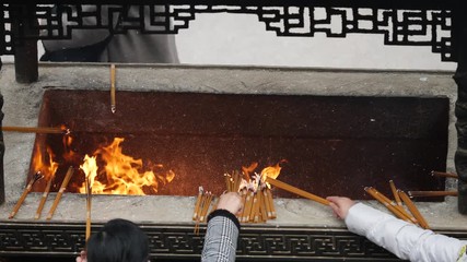 Slow motion fire and incense smoke in traditional Chinese temple, prayers put burning incense into incense burner, 4K video.