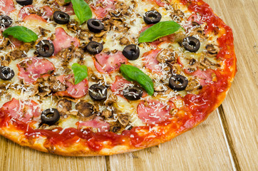 Pizza with ham, mushrooms and olives on wooden surface.