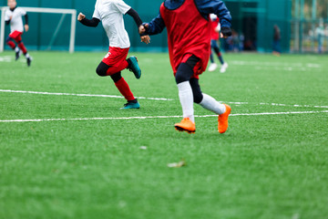 Boys in red white sportswear running on soccer field. Young footballers dribble and kick football ball in game. Training, active lifestyle, sport, children activity concept 