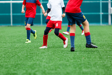Boys in red white sportswear running on soccer field. Young footballers dribble and kick football ball in game. Training, active lifestyle, sport, children activity concept