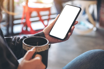 Mockup image of a hand holding black mobile phone with blank screen while drinking coffee in cafe
