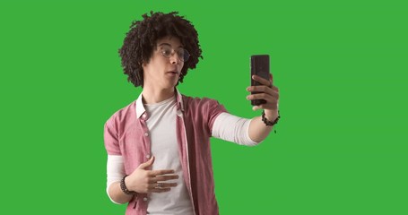 Young man with curly hair using mobile phone for video call over green background
