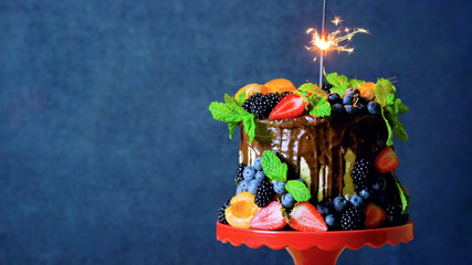 Delicious chocolate drip cake decorated with fresh seasonal fruit and berries with burning...