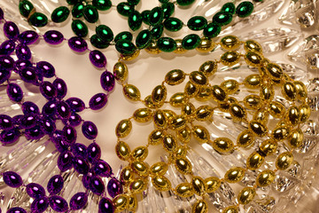 Close up view of shiny green, purple and gold Mardi Gras beads on a white crystal glass background