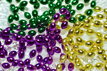 Close up view of shiny green, purple and gold Mardi Gras beads on a white crystal glass background